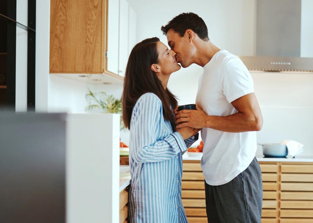 A couple kissing in the kitchen.